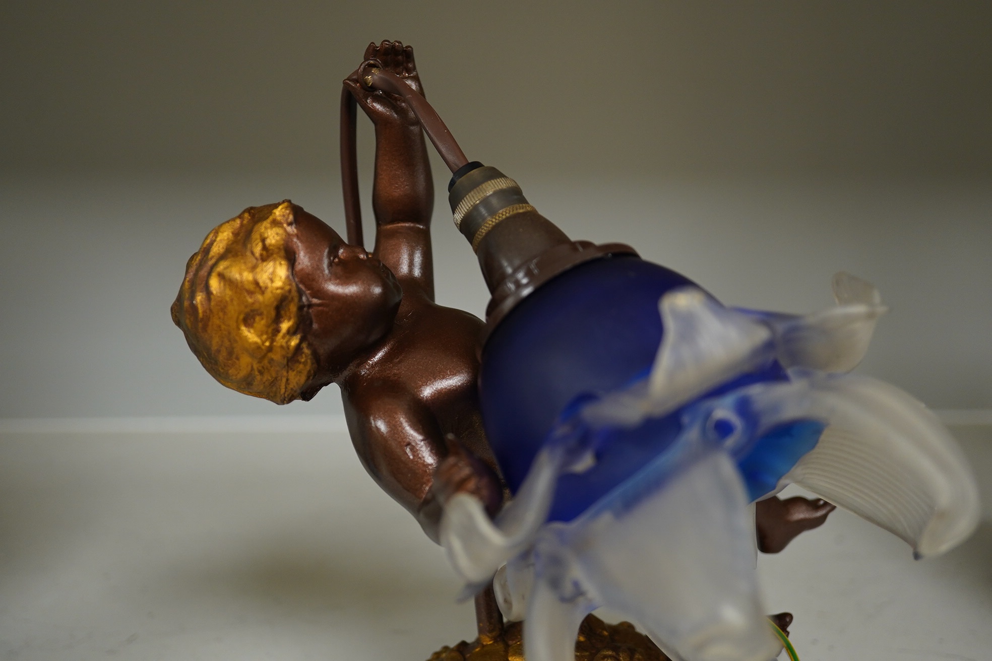 A French bronzed gilded wall light cherub with blue and frosted glass petal shade, circa 1920’s, wired, projection, 24cm. Condition - good